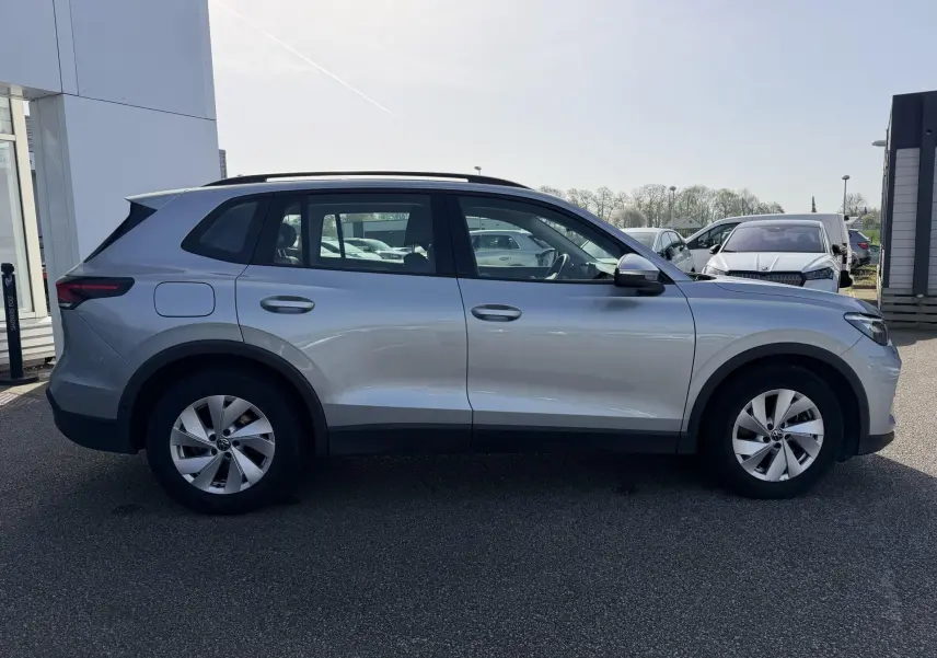 Vue de profil côté gauche d'un Volkswagen Tiguan gris 2025 garé en extérieur, avec jantes alliage et toit noir.