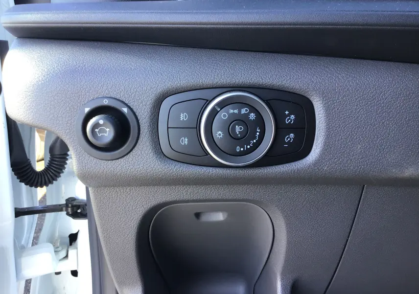 Détail des commandes d'éclairage et réglage des rétroviseurs côté gauche du tableau de bord du Ford Transit blanc 2024.