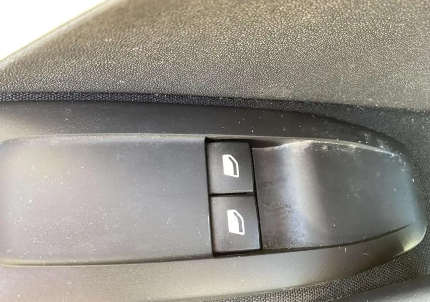 Gros plan sur les boutons de lève-vitres avant électriques noirs dans une Peugeot 208 noire de 2015.