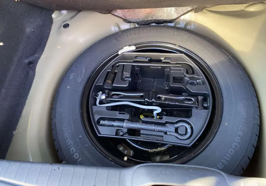 Roue de secours acier 15 pouces avec outils de bord dans le coffre d'une Peugeot 208 noire de 2015.