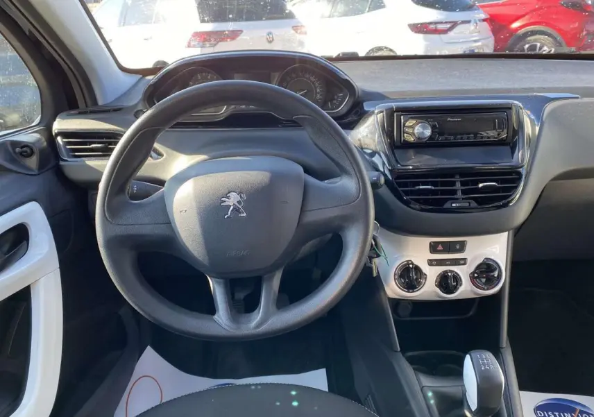 Vue intérieure du poste de conduite d'une Peugeot 208 noire de 2015, avec volant, tableau de bord et autoradio Pioneer visible.