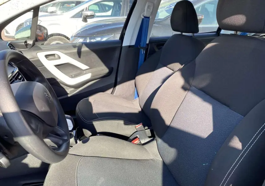 Intérieur avant droit de la Peugeot 208 noire 2015, sièges tissu gris et volant visible côté conducteur.