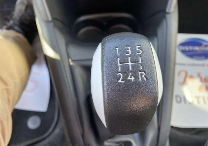 Le levier de vitesses manuel noir et blanc de la Peugeot 208 essence, vue en gros plan depuis l'intérieur.