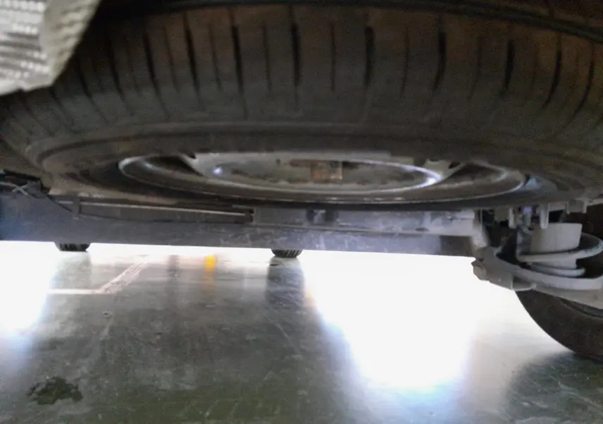 Vue en contre-plongée sous un Renault Express Van blanc 2023, montrant la roue de secours et la suspension arrière.