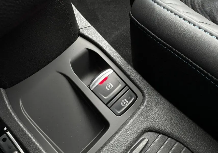 Gros plan sur la console centrale noire avec frein de parking électrique et accoudoir gris à surpiqûres bleues Renault Clio 2025.