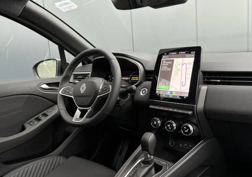 Vue intérieure côté conducteur de la Renault Clio 2025 avec tableau de bord noir et écran tactile central vertical.