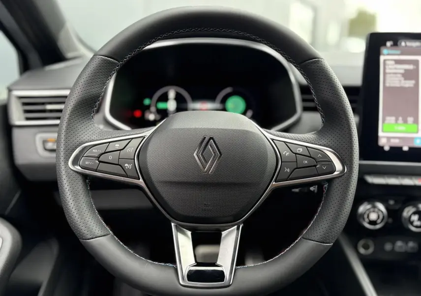 Volant en cuir noir perforé avec surpiqûres bleues de la Renault Clio E-Tech Gris Rafale, tableau de bord et écran tactile visibles.
