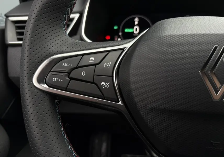 Gros plan sur les commandes du volant côté gauche d'une Renault Clio gris Rafale, avec surpiqûres bleues visibles.