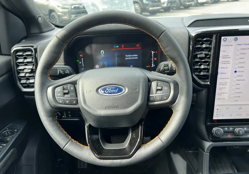 Vue intérieure centrée sur le volant cuir noir avec surpiqûres orange du Ford Ranger 2025, tableau de bord digital et écran tactile.
