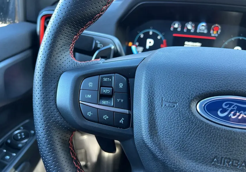Gros plan sur le volant en cuir noir avec surpiqûres rouges du Ford Ranger Raptor 2025, boutons multifonctions visibles.