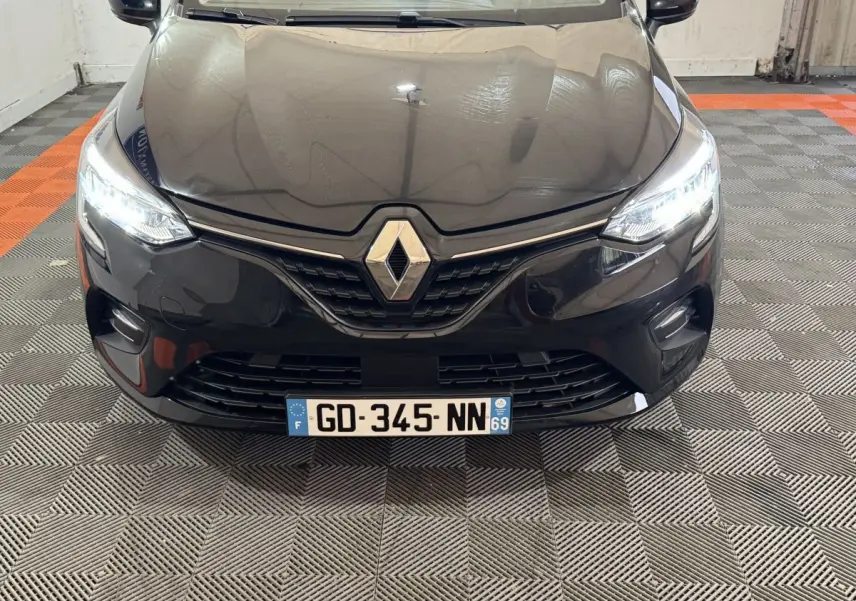 Vue avant rapprochée d’une Renault Clio Business E-Tech hybride noire avec phares LED allumés dans un garage.