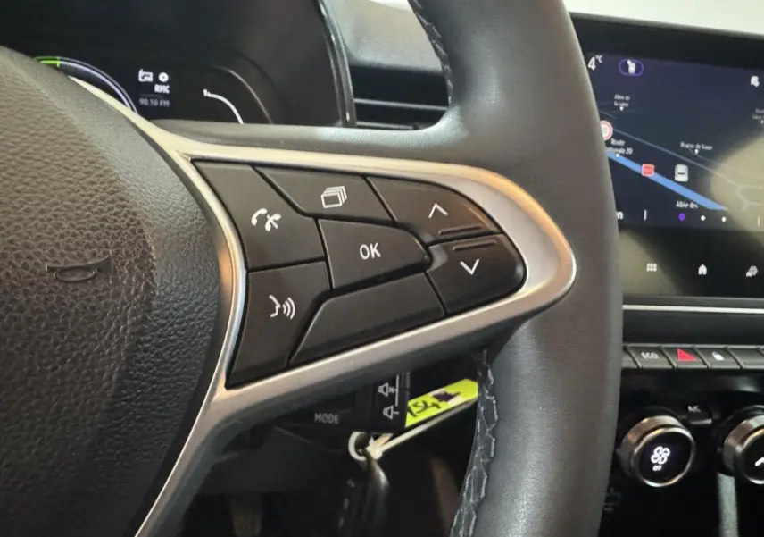 Gros plan sur le volant cuir synthétique noir de la Renault Clio Business E-Tech avec commandes multifonctions et écran tactile en arrière-plan.