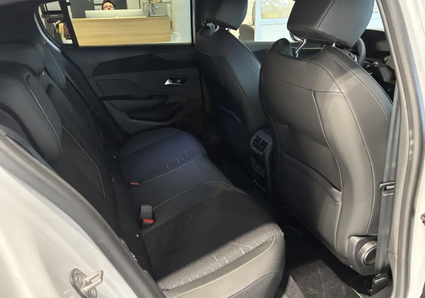 Vue intérieure arrière côté gauche de la Peugeot 308 blanche 1.2i Hybrid avec sellerie noire et surpiqûres vert Adamite.