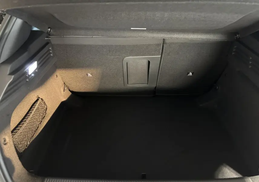 Coffre ouvert de la Peugeot 308 blanche, vue intérieure montrant un espace de rangement noir et un filet latéral.