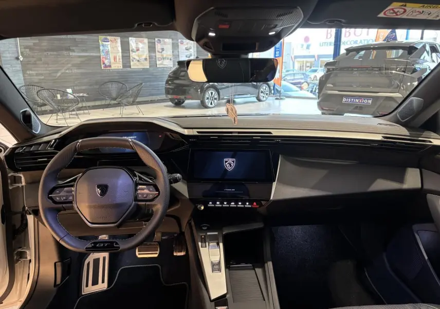 Vue intérieure avant de la Peugeot 308 blanche, volant GT compact, écran tactile central et pédalier aluminium sport.