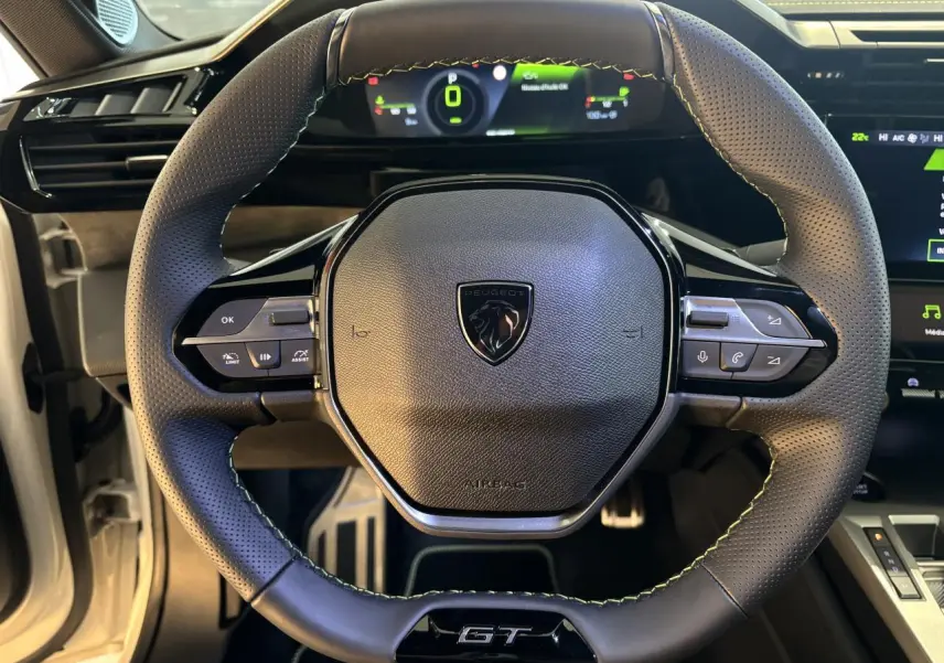 Volant GT en cuir perforé avec surpiqûres vert Adamite et logo Peugeot, vue centrée sur le poste de conduite.
