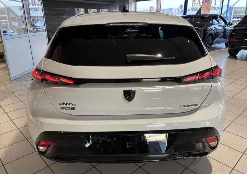 Vue arrière d'une Peugeot 308 hybride blanche avec feux arrière LED en forme de griffes et bandeau noir brillant.