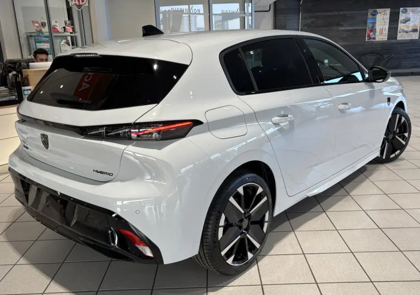 Vue 3/4 arrière droite d'une Peugeot 308 Hybrid blanche avec jantes alliage bicolores et vitres teintées.