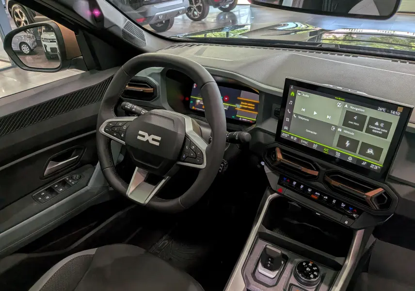 Vue intérieure côté conducteur du Dacia Bigster Hybrid-G 150 4x4 gris, avec tableau de bord numérique et écran tactile central.