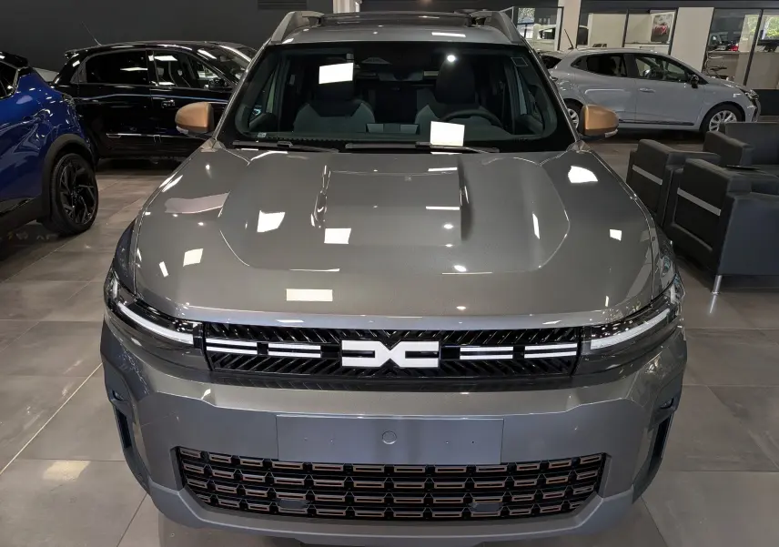 Vue frontale du Dacia Bigster Hybrid-G 150 4x4 gris schiste avec calandre noire et détails cuivrés en showroom.