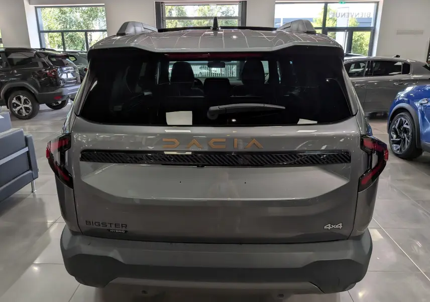 Vue arrière du Dacia Bigster Hybrid-G 150 4x4 gris schiste, avec logo doré et feux arrière noirs en intérieur showroom.