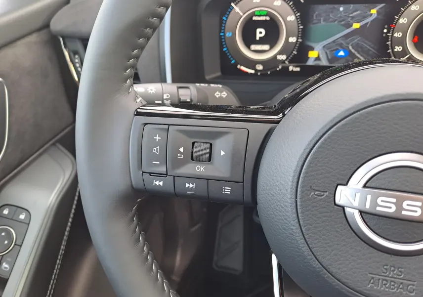 Gros plan sur le volant noir du Nissan Qashqai 2025 avec commandes intégrées et tableau de bord numérique en arrière-plan.