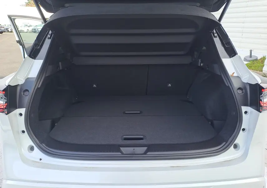 Coffre ouvert vu de l'arrière d'un Nissan Qashqai blanc nacré avec toit noir, montrant un espace de chargement spacieux.