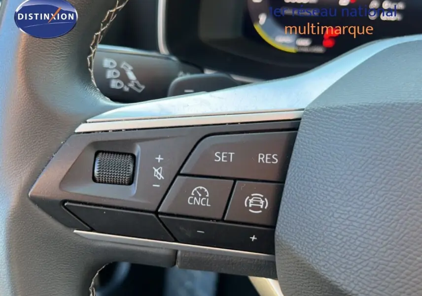 Gros plan sur les commandes au volant à gauche d'une SEAT LEON gris magnétique 2025, avec régulateur de vitesse et volume.