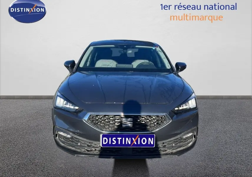 Vue frontale d'une SEAT Leon gris magnétique métal 2025 avec calandre hexagonale et phares LED allumés.