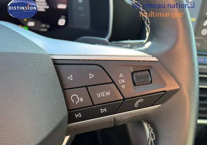 Gros plan sur les commandes au volant côté gauche d'une SEAT Leon gris magnétique, avec boutons multifonctions visibles.