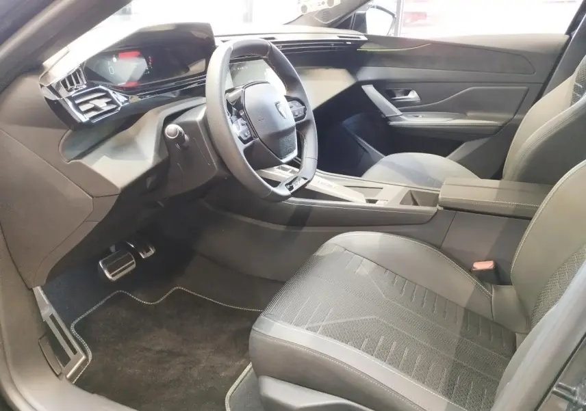 Intérieur avant droit de la Peugeot 308 1.2i Hybrid 2026 avec sièges noirs et volant compact GT cuir.