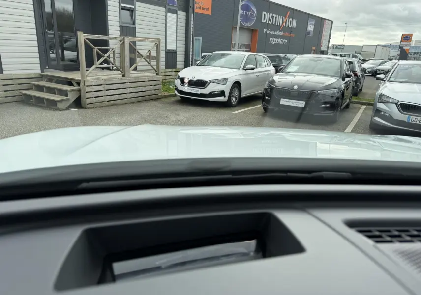 Vue depuis l'intérieur du Volkswagen Tiguan blanc, montrant le capot et un parking avec plusieurs voitures devant.