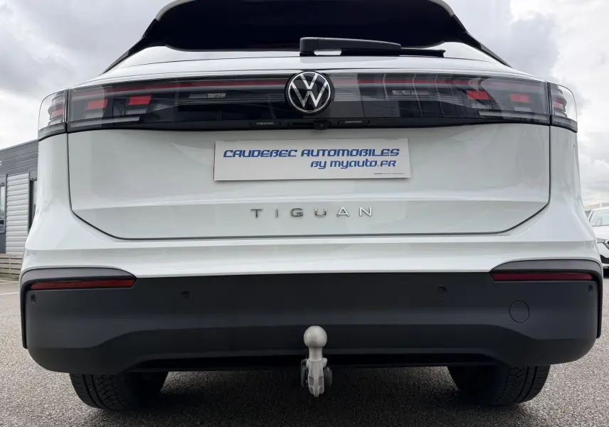 Vue arrière d'un Volkswagen Tiguan blanc avec attelage rabattable et feux arrière LED noirs.