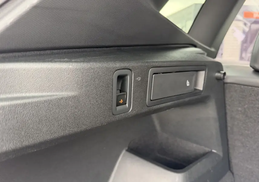 Détail intérieur du coffre du Volkswagen Tiguan 2025, montrant la commande électrique de rabattement des sièges en plastique noir.