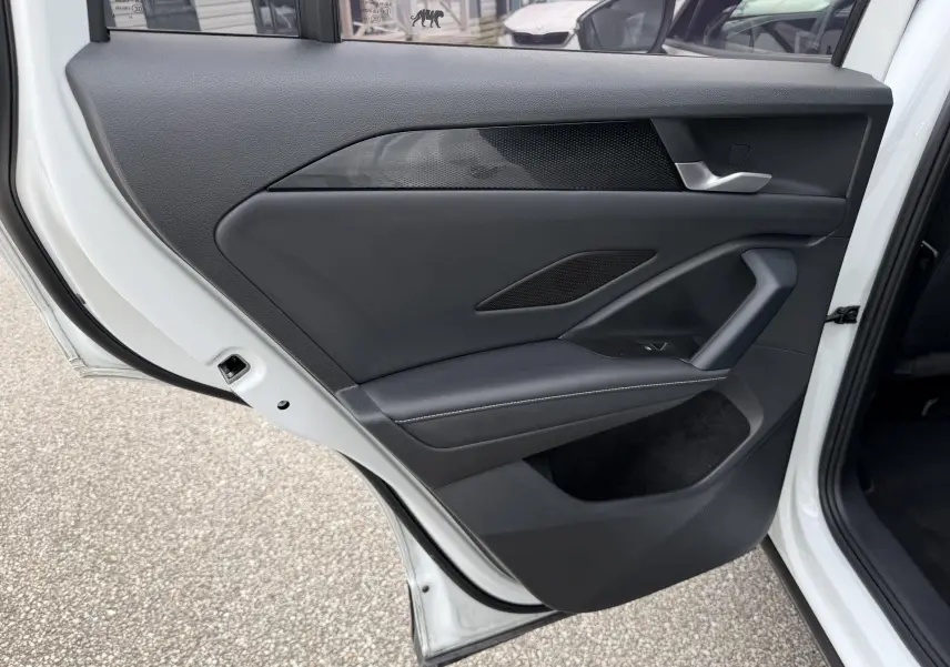 Vue rapprochée de la porte arrière gauche ouverte d’un Volkswagen Tiguan blanc, avec garniture intérieure noire et poignée argentée.