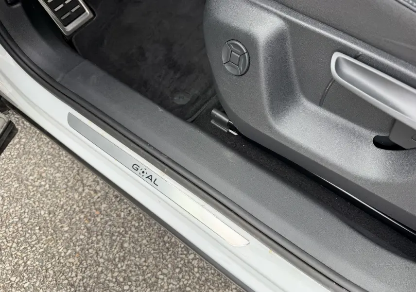 Gros plan sur la porte côté conducteur d’un Volkswagen Tiguan blanc, montrant la molette de réglage du siège et le seuil de porte.