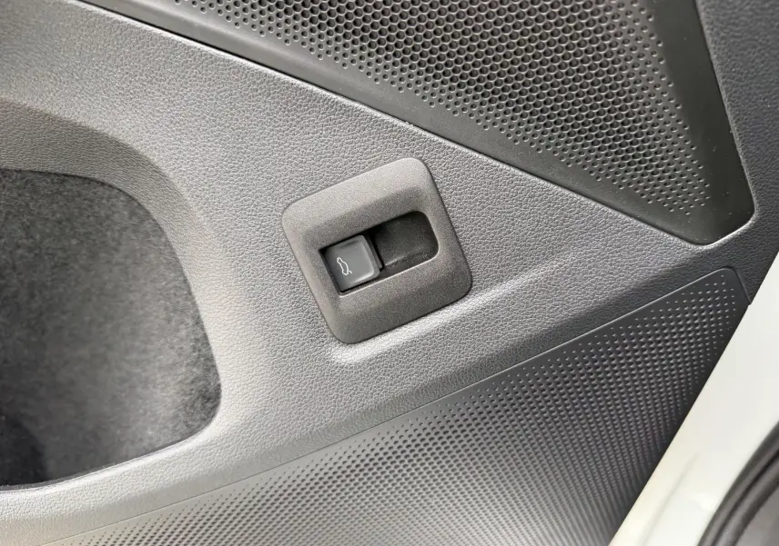 Gros plan sur le bouton d'ouverture électrique du hayon, côté droit intérieur d'un Volkswagen Tiguan blanc.
