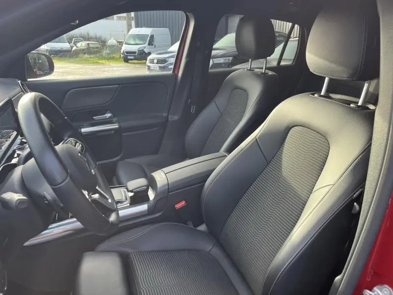 Vue intérieure côté conducteur du Mercedes GLA 200 rouge Patagonie, sièges en tissu/similicuir noir avec volant cuir multifonction.