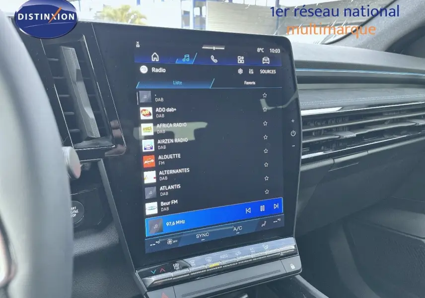 Vue intérieure centrée sur l'écran tactile du tableau de bord du Renault Austral blanc nacré 2025, affichant les stations radio.