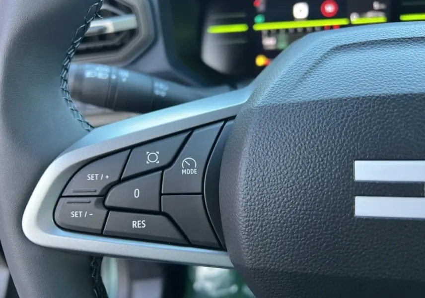 Gros plan sur les commandes au volant à gauche du Dacia Duster 2025, version mild hybrid vert cèdre.