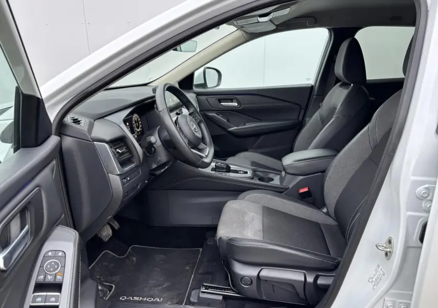Vue intérieure côté conducteur du Nissan Qashqai blanc nacré 2025, avec sellerie mixte noire et tableau de bord moderne.