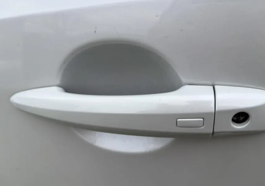 Poignée de porte blanche nacrée du Nissan Qashqai III 2025 vue de près, avec bouton de déverrouillage intégré.
