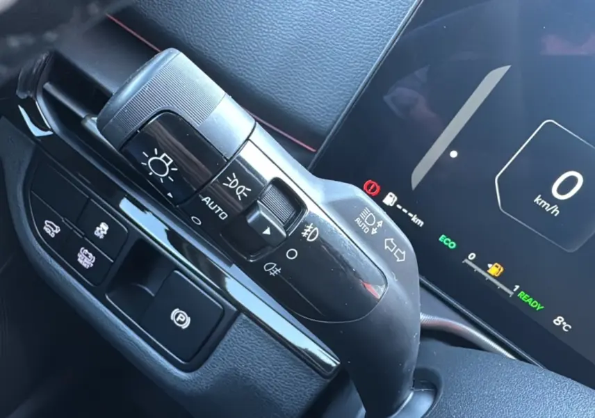 Gros plan sur la commande d’éclairage et tableau de bord numérique du Kia Sportage noir étoilé, affichant 0 km/h et mode ECO.