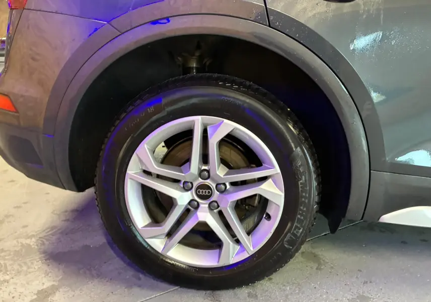 Gros plan sur la roue arrière droite d’un Audi Q5 gris 2024 avec jante aluminium 5 branches doubles.