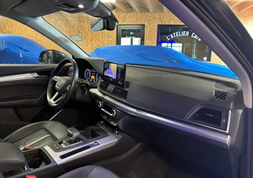 Intérieur de l'Audi Q5 2024 vu côté conducteur, tableau de bord noir avec écran central et volant cuir multifonction.