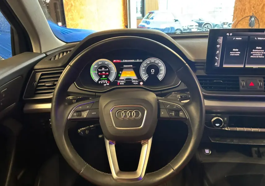 Vue intérieure centrée sur le volant cuir noir et le tableau de bord digital de l'Audi Q5 hybride rechargeable 2024.