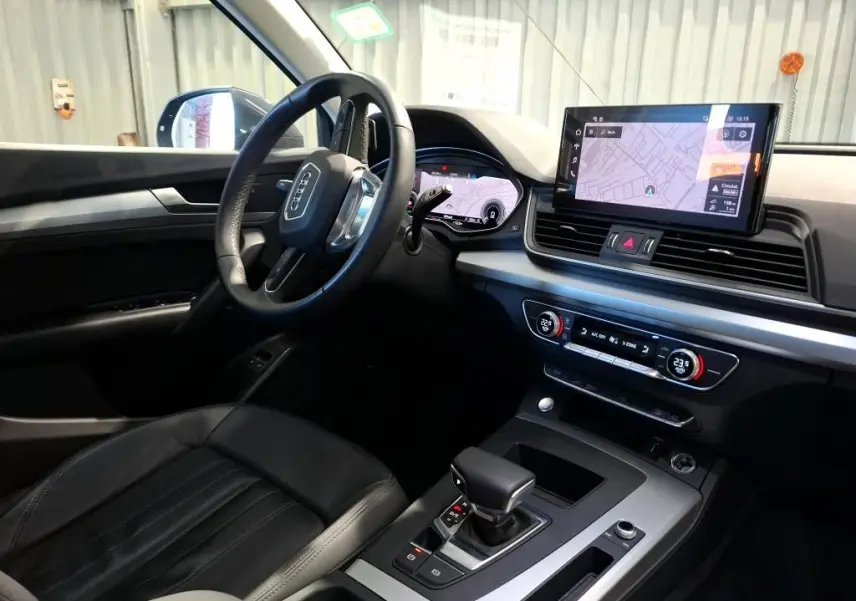 Audi Q5 gris en vue 3/4 arrière droit, avec jantes 5 branches doubles et crochet d'attelage visible.