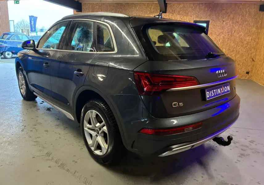Audi Q5 gris en vue 3/4 arrière droit, avec jantes 5 branches doubles et crochet d'attelage escamotable visible.