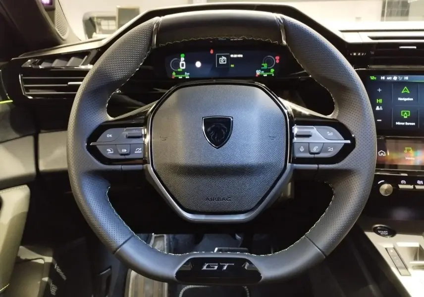 Vue rapprochée du volant compact GT en cuir avec surpiqûres vert Adamite et combiné numérique du Peugeot 308 Hybrid 2026.