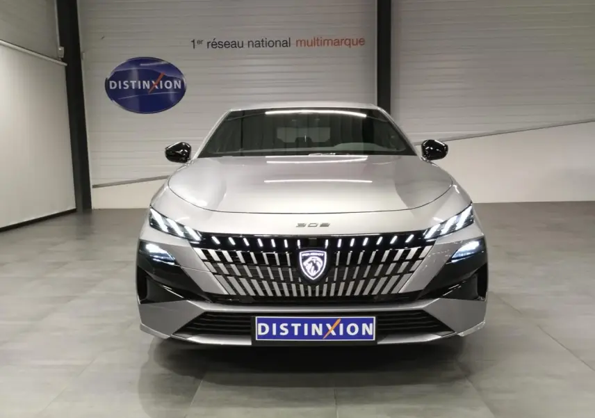 Vue avant d'une Peugeot 308 gris Artense avec calandre illuminée et phares LED allumés en intérieur showroom.